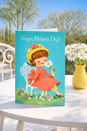 A Mother's Day greeting card featuring a young girl in a red dress holding a flower, sitting on a chair in a garden setting with a vase of white flowers nearby.