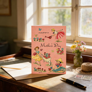 A pink greeting card with illustrations of women engaged in various activities, such as gardening, is displayed on a wooden desk near a window.