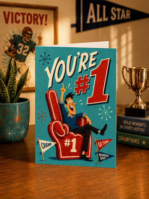 a card with a cartoon character sitting in a red chair, celebrating a victory. The card has a blue background with a red and white design, and the text "YOU'RE #1" is prominently displayed. In the background, there is a trophy and a framed picture of a football player.