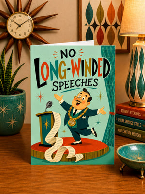 a card with a cartoon illustration of a man standing at a podium and holding a microphone, with a large text that reads "NO LONG-WIDENED SPEECES". The card is placed on a wooden surface, surrounded by various decorative items such as a clock, a lamp, and a bowl.