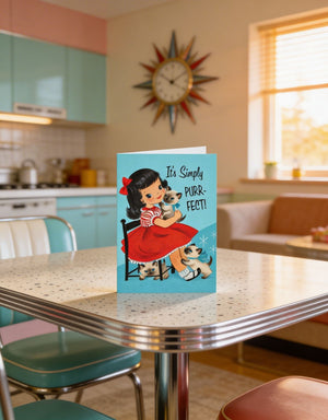 A vintage-style greeting card featuring a young girl with a cat, placed on a retro-style dining table in a retro-style kitchen.