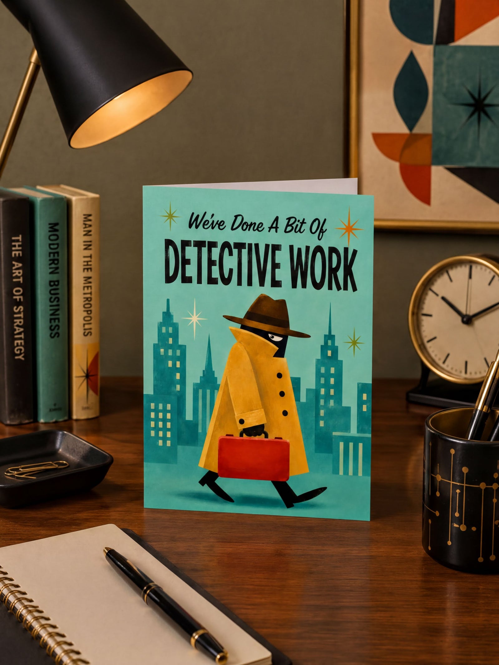 A folded greeting card shown standing upright on a white background. The card features a stylized detective character in a yellow trench coat and brown hat walking with a red suitcase against a teal city skyline.