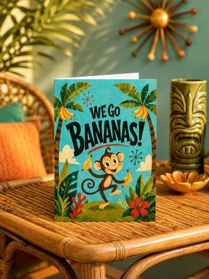 A greeting card with a monkey holding bananas, surrounded by tropical elements, sits on a wooden table.