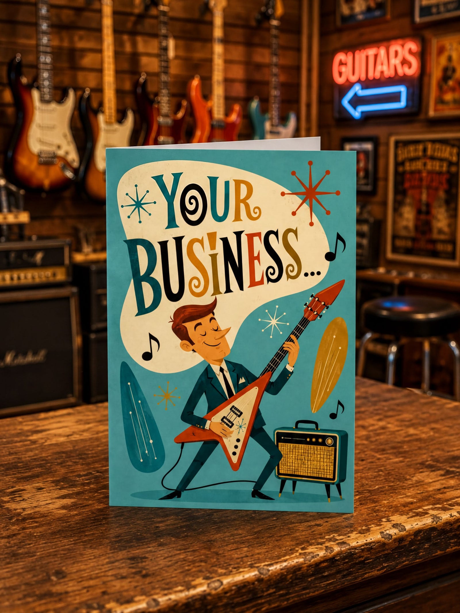 A folded greeting card shown front-on against a white background. The card features a retro-style illustration of a man playing an electric guitar with an amplifier, under a large cream speech bubble that reads “YOUR BUSINESS.