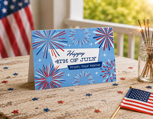 A patriotic 4th of July greeting card with a blue background and red, white, and blue fireworks design, placed on a wooden table with a jar of sparklers and an American flag in the background.