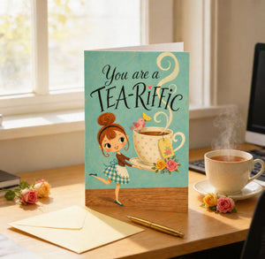 A greeting card with a girl holding a teacup and flowers, sitting on a desk with a cup of tea and a pen.