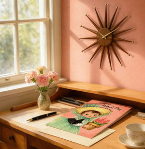a desk with a card, a vase of flowers, a clock, and a pen, all arranged neatly on the surface.