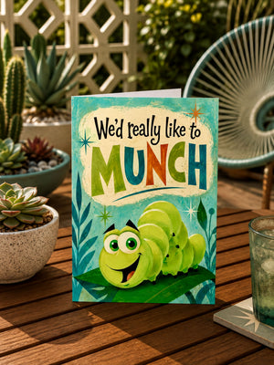 A colorful greeting card with a cartoon caterpillar on a leaf, placed on a wooden table with potted plants in the background.