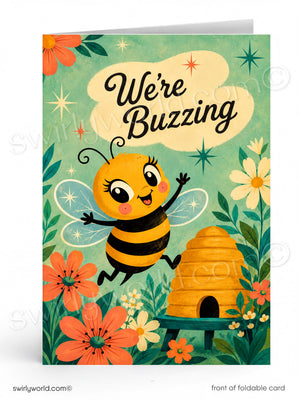 A folded greeting card shown front-facing on a white background. The card features a cute cartoon bee with the text 'We're Buzzing' above it, surrounded by flowers, leaves, stars, and a beehive.