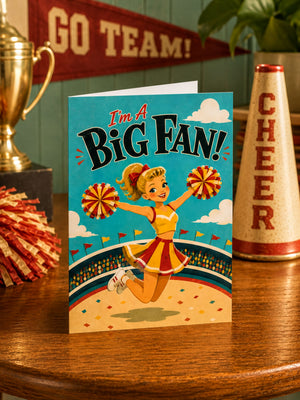 a cheerleader holding pom-poms, with a card in the foreground that says "I'm a Big Fan!" and a trophy and a cheerleader cone in the background.