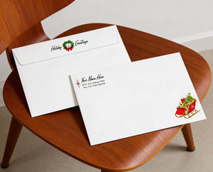 two white envelopes with holiday greetings and a Christmas-themed design, placed on a wooden chair.