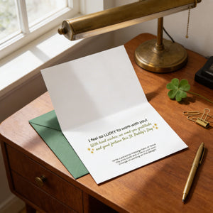 a greeting card with a personal message, placed on a wooden desk next to a lamp and some office supplies.