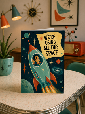 A retro-themed greeting card featuring a cartoon rocket ship and planets with the text 'WE'RE USING ALL THIS SPACE.