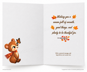 An open greeting card with a white background, featuring a brown cartoon bear wearing a red plaid scarf and a butterfly on its head on the left panel, and autumn-themed decorative text on the right panel.