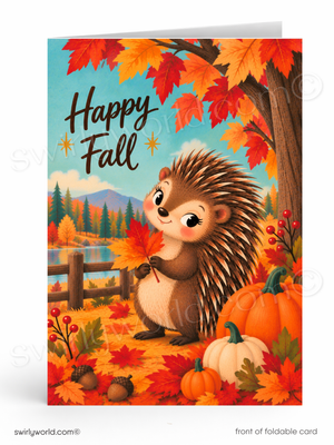 A folded greeting card shown front-on against a white background. The card features a whimsical autumn illustration with a smiling hedgehog standing among orange pumpkins, red and yellow leaves, acorns, and a tree trunk, with the words “Happy Fall” in large script near the top left.