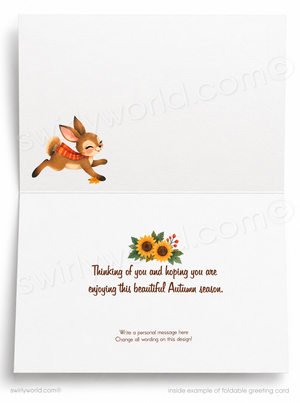 Foldable greeting card shown open, with a small autumn-themed illustration of a brown bunny wearing an orange scarf on the upper panel and a sunflower cluster above brown handwritten text on the lower panel. The card is photographed against a light gray background with faint watermark text across the image.