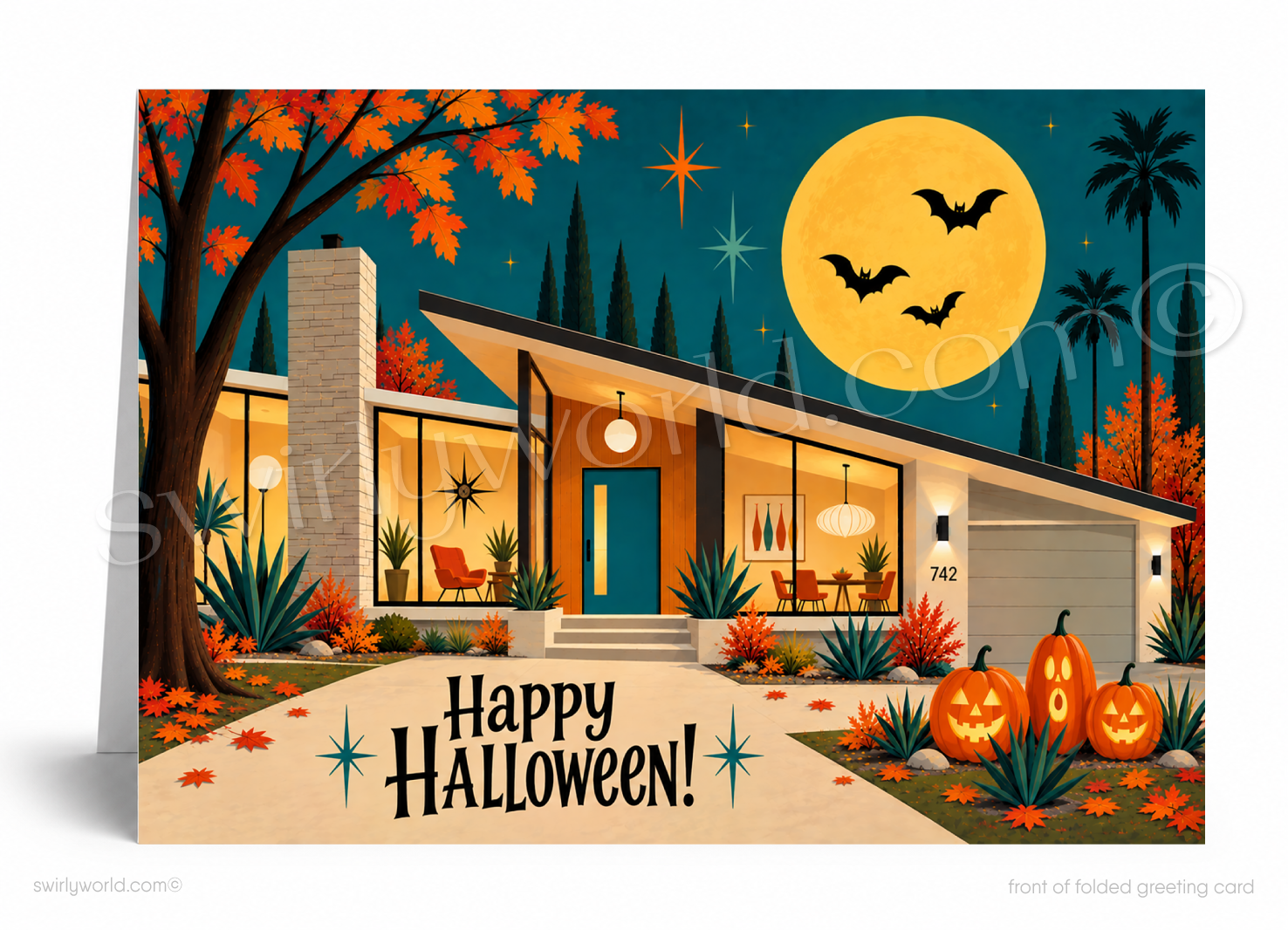 A folded greeting card shown standing upright, featuring a stylized mid-century modern house at night with autumn trees, a large yellow moon, bats, jack-o'-lanterns, and the text 'Happy Halloween!'.