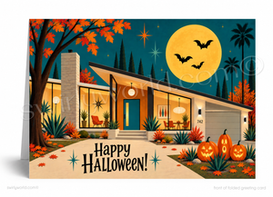 A folded greeting card shown standing upright, featuring a stylized mid-century modern house at night with autumn trees, a large yellow moon, bats, jack-o'-lanterns, and the text 'Happy Halloween!'.