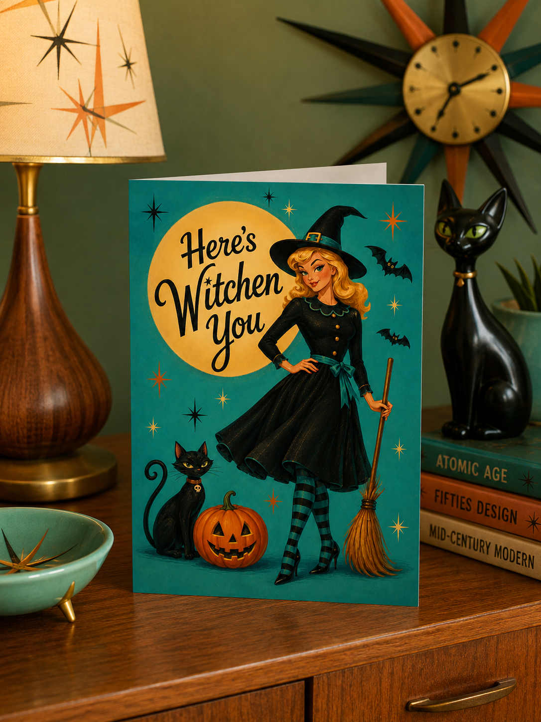 A Halloween-themed foldable greeting card featuring a retro illustration of a blonde witch in a black dress and hat, standing beside a broom, black cat, and jack-o'-lantern in front of a large yellow moon on a teal background. The card reads 'Here's Witchen You'.