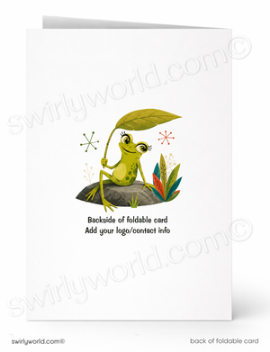 A folded white card shown front and back on a white background. The front features a whimsical illustration of a green frog sitting on a rock under a large green leaf, with small plants and sparkles.
