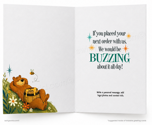 An open greeting card with a white background. The left panel shows a brown bear lying in grass among flowers and holding a small basket, with a bee nearby.