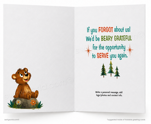 An open greeting card shown front and center on a white background. The left page features a cartoon brown bear sitting on a rock with small flowers at its feet.