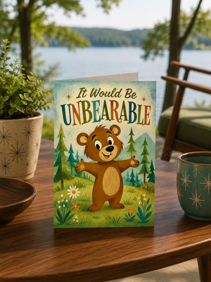 A greeting card featuring a cartoon brown bear in a forest with the text 'It Would Be UNBEARABLE' stands on a wooden table in a cozy outdoor patio setting with a potted plant, bowl, mug, and blurred lake background.
