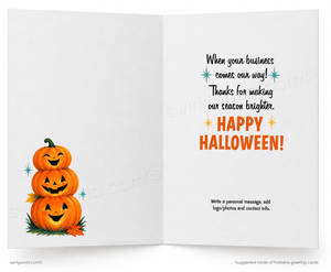 An open white greeting card with Halloween-themed printed text on the right side and a stack of three smiling pumpkins on the left side, shown on a light gray background.