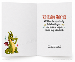 An open greeting card with a white interior. The left panel shows a green cartoon dragon with red wings and a yellow belly pointing upward.